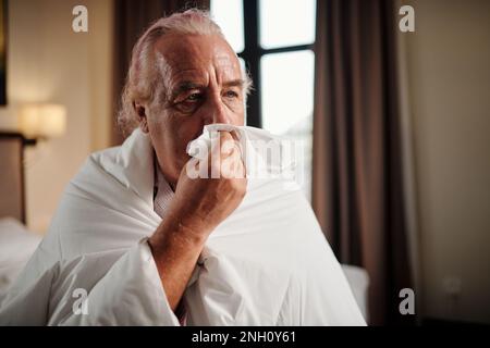 Ritratto di uomo anziano avvolto in piumino e naso che soffia Foto Stock