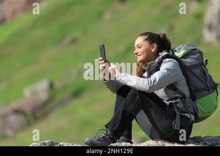 Buon escursionista che utilizza uno smartphone seduto in natura Foto Stock