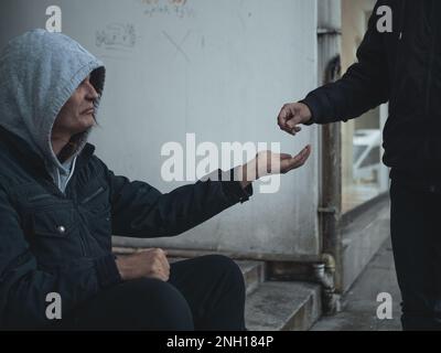 L'uomo senza casa si siede sui gradini e chiede aiuto e denaro. Foto Stock