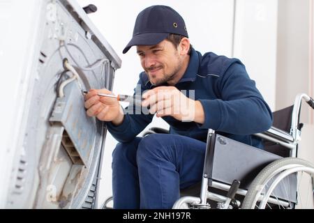 l'operatore disabile lavora idraulico ripara una lavatrice in lavanderia Foto Stock