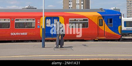 Clapham Junction stazione ferroviaria piattaforma di lavoro uomo d'affari in attesa sulla piattaforma raccoglie valigetta Sud Ovest treni servizio arriva per Londra UK Foto Stock