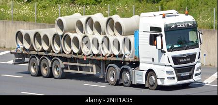 Primo piano MAN bianco autocarro hgv traino di rimorchi a piattaforma piatta carico articolato di tubi di grande diametro di tipo di drenaggio in calcestruzzo prefabbricato su autostrada nel Regno Unito Foto Stock