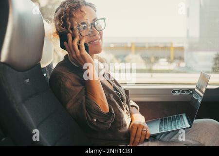 Comunicazione e concetto di viaggio stile di vita professionale. La donna moderna sorride e usa il telefono cellulare seduto su un sedile dell'autobus come passeggero di viaggio. Persone e comp Foto Stock