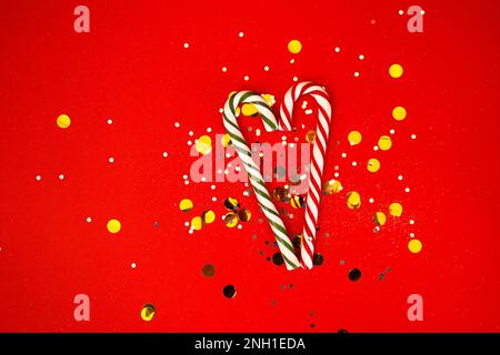 Due caramelle dolci di canna formano una forma di cuore. Sfondo rosso brillante con argento luccichio e coriandoli. Giornata Vatentina o concetto di Natale. Posto libero per Foto Stock