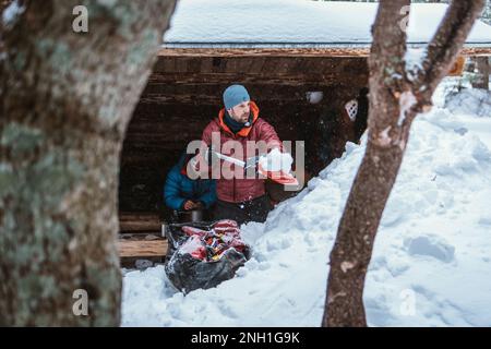 Uomo che in inverno spala la neve davanti alla cabina Foto Stock