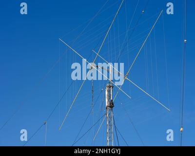 Un primo piano di un'antenna radio HAM con corde di appoggio contro un cielo blu Foto Stock