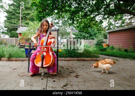 Un bambino piccolo gioca il violoncello per il suo pollo dell'animale domestico fuori Foto Stock