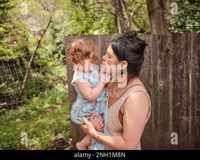 Mamma e figlia abbracciano e mostrano affetto in recintato in cortile Foto Stock