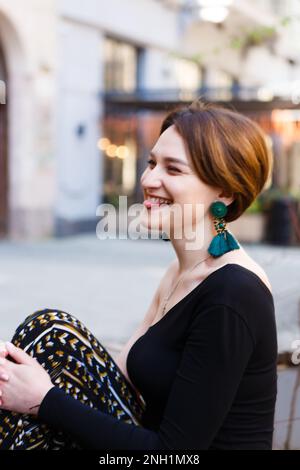 giovane donna elegante dai capelli rossi ride seduto sul vicolo della città in estate Foto Stock