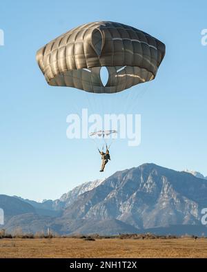 Un paracadutista dell'esercito italiano con la Brigata Paracadutisti 'Folgore' si prepara ad atterrare mentre conduce un'operazione aerea accanto agli Stati Uniti Paracadutisti dell'esercito assegnati alla Brigata aerea 173rd nella zona di caduta di Frida a Pordenone, 7 dicembre 2022. La Brigata Airborne 173rd è la U.S.A. La forza di risposta di contingenza dell'esercito in Europa, che fornisce le forze rapidamente dispiegabili alle aree di responsabilità europee, africane e del comando centrale degli Stati Uniti. Schierata in avanti in Italia e Germania, la brigata si allena regolarmente insieme agli alleati e ai partner della NATO per costruire partnership e streng Foto Stock