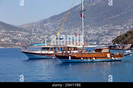 Barche (gulets) ormeggiate nella baia di Kalkan con il villaggio di Kalkan sullo sfondo, Turchia. Luglio 2022 Foto Stock