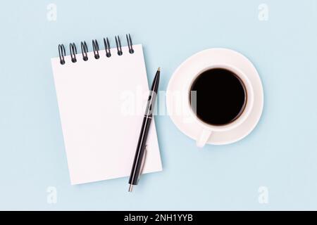 Tazza di caffè nero e taccuino vuoto su sfondo blu. Concetto minimo con spazio di copia. Foto Stock