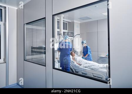 Due medici che frequentano una donna paziente in reparto ospedaliero. ICU Foto Stock