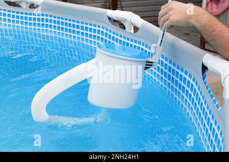 L'uomo pulisce lo skimmer per la piscina di telaio. Pulizia piscina contaminata. Foto Stock