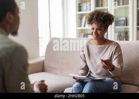 Sorridente amichevole donna nera psicologa che ha conversazione con paziente Foto Stock