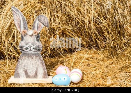 Coniglio di legno su fondo fieno con uova di Pasqua dipinte. Pasqua, una cartolina con un posto per il testo. Foto di alta qualità Foto Stock