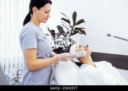 Ritratto di giovane donna rilassato ottenere SMAS ultrasuoni viso sollevamento massaggio con attrezzature professionali in centro di bellezza Foto Stock