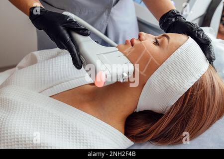 Ritratto di giovane donna rilassato ottenere SMAS ultrasuoni viso sollevamento massaggio con attrezzature professionali in centro di bellezza Foto Stock