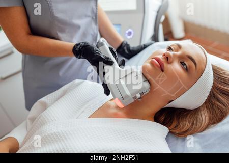 Ritratto di giovane donna rilassato ottenere SMAS ultrasuoni viso sollevamento massaggio con attrezzature professionali in centro di bellezza Foto Stock