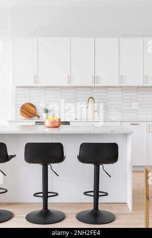 Una bella cucina particolare con armadi bianchi, un rubinetto d'oro, marrone picket piastrelle in ceramica backsplash, e sgabelli nero bar seduti su un'isola. Foto Stock