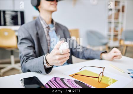 Primo piano di un giovane uomo che indossa il visore VR e tiene il controller mentre lavora a un progetto di realtà coinvolgente Foto Stock