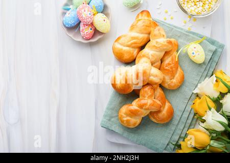 Colazione di Pasqua, concetto di Holliday. Panini di coniglietto pasquale con cannella a base di pasta di lievito con smalto arancione, decorazioni pasquali, uova colorate Foto Stock