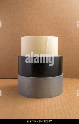 Tre diversi tipi di rotoli di nastro impilati con lo sfondo marrone della scatola di cartone Foto Stock