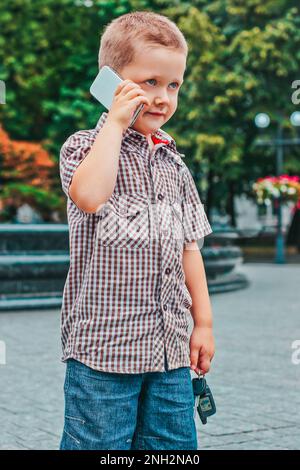 Chernihiv, Ucraina - 15 agosto 2014: Bambino che parla al telefono. Un ragazzino tiene in mano le chiavi dell'auto. Piccolo capo. Foto Stock