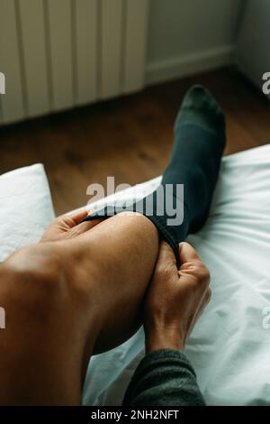un uomo si mette su un calzino a compressione seduto sul letto di casa Foto Stock