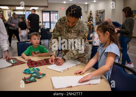Il Sgt. Catrecia Stubbs, 7th Component Maintenance Squadron NCO responsabile del comandante di stato maggiore di supporto, mostra a un bambino militare come spianare il loro tessuto di calza alla Dyess Air Force base, Texas, 8 dicembre 2022. Dopo aver scelto il loro tessuto, i bambini militari hanno attraversato più stazioni, mentre gli è stato insegnato come le loro calze natalizie sono state messe insieme prima di essere completate. Dopo aver ricevuto le calze, i bambini sono stati anche in grado di scegliere i tessuti per creare calze per un bambino adottivo nella comunità locale. tessuti,vacanze,bambini militari,calze, Foto Stock