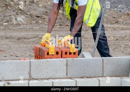 Muratore duro posa mattoni su cemento mix in cantiere. Combattere la crisi immobiliare costruendo case più accessibili concetto Foto Stock