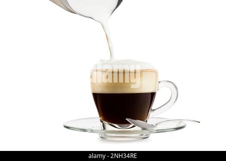 Preparazione del cappuccino in una tazza di vetro con pannarello su sfondo bianco. Foto Stock