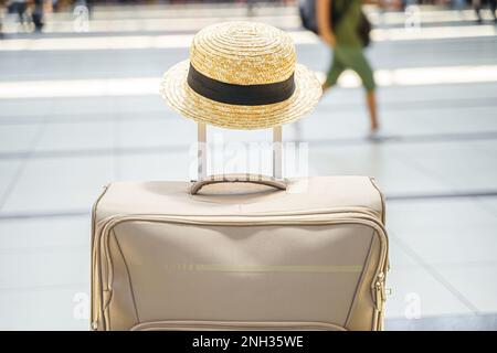 Cappello di paglia sulla valigia grande, borsa nel terminal dell'aeroporto. In attesa dell'imbarco per il volo. Vacanza in famiglia. Check-in bagagli nella sala delle partenze. S Foto Stock