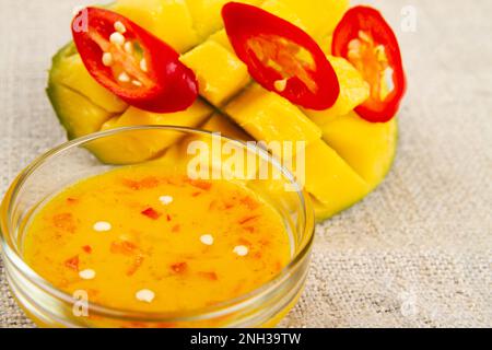 Primo piano di anelli di peperoncino rosso, metà tagliata di mango e marmellata di peperoncino di mango su un panno rustico. Messa a fuoco morbida Foto Stock