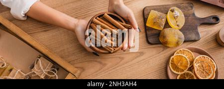 vista dall'alto di una femmina afroamericana tagliata che tiene la ciotola con bastoncini di cannella vicino a saponette e fette di arancia essiccate, banner, immagine stock Foto Stock