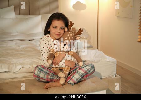 Bambina con cervo giocattolo in camera da letto illuminata da lampada da notte Foto Stock