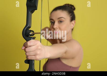 Donna con arco e freccia pratica tiro con l'arco su sfondo giallo, fuoco a portata di mano Foto Stock