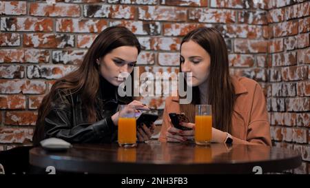 Due belle ragazze sono seduti in un caffè e parlare con i telefoni. Foto Stock