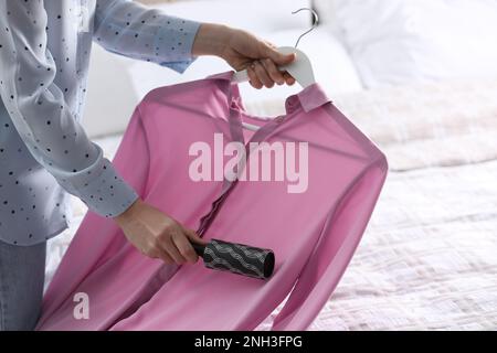 Giovane donna che pulisce i vestiti con il rullo di lanugine a casa, primo piano Foto Stock