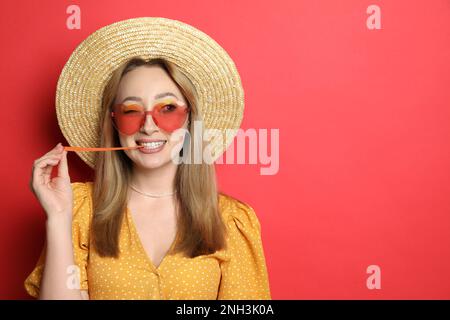 Giovane donna alla moda masticare bubblegum su sfondo rosso, spazio per il testo Foto Stock