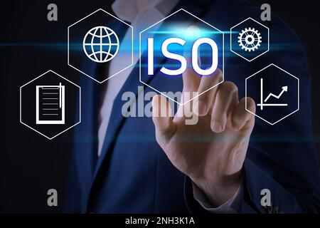 Uomo d'affari che punta all'icona virtuale con testo ISO su sfondo scuro, primo piano Foto Stock
