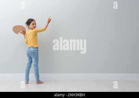 Piccola ragazza pittura su parete grigio chiaro al coperto. Spazio per il testo Foto Stock