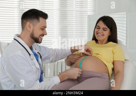 Medico che misura il ventre della donna incinta con nastro adesivo in clinica Foto Stock