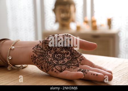 Donna con tatuaggio all'henné sul palmo della mano a tavola all'interno, primo piano. Tradizionale ornamento di mehndi Foto Stock