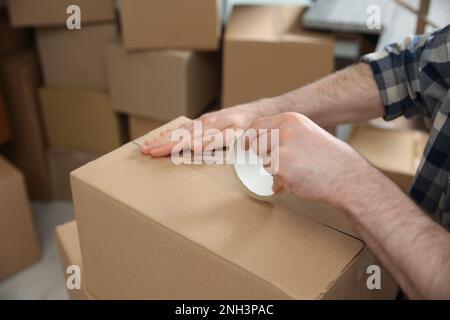 Uomo che nastrano scatola di cartone all'interno, primo piano. Giorno in movimento Foto Stock