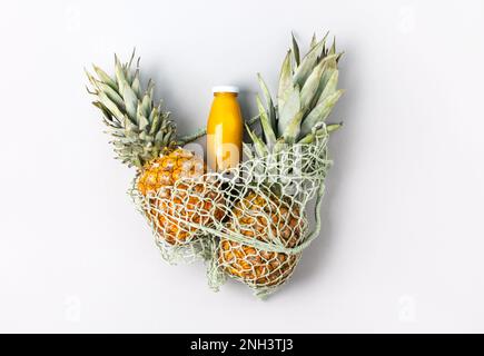 Due ananas maturi e succosi e succo naturale di ananas fresco in una bottiglia di vetro su sfondo grigio in una busta verde. Sano, disintossicante e dietetico n Foto Stock