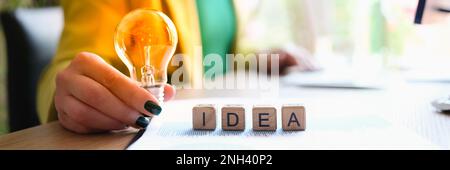 Donna d'affari in tuta verde che tiene lampadina sopra idea closeup parola Foto Stock