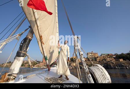 Uomo egiziano in tradizionale garb boatmens su una felucca o barca a vela tradizionale sul Nilo, Assuan, Egitto Foto Stock