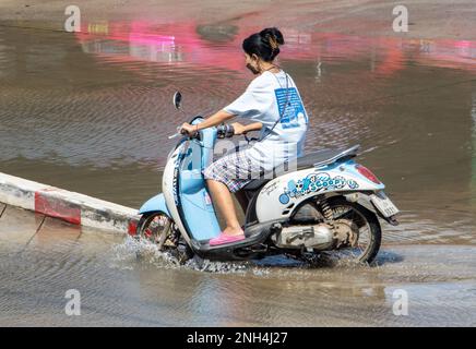 SAMUT PRAKAN, THAILANDIA, 25 2023 GENNAIO, Una donna con maschera facciale cavalca una moto attraverso pozza Foto Stock