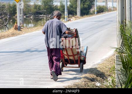 Un vecchio uomo che spinge un carrello con un carico di materiale riciclabile Foto Stock